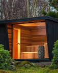 Modern outdoor cabin with wooden interior and black exterior, surrounded by trees and greenery.