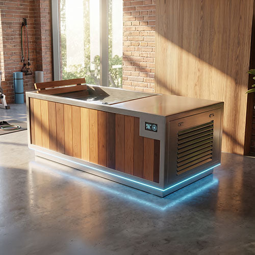 A modern plunge tub with a wood-paneled front, stainless steel top and trim, and integrated blue LED under-glow lighting, shown in a rustic indoor-outdoor space with brick and wood walls.