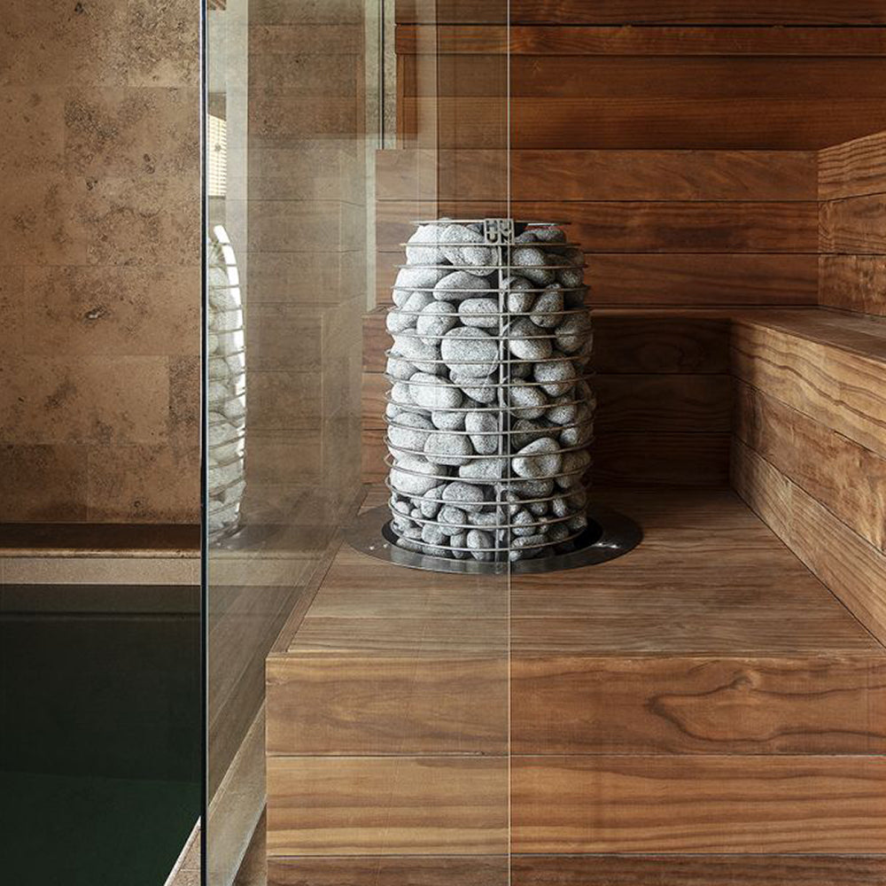 Wooden sauna with a stack of stones inside, surrounded by wooden benches and walls and a glass wall next to a pool