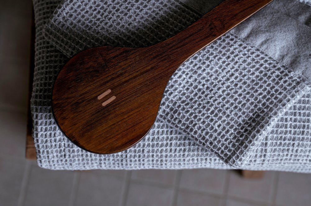 A close-up of a dark brown wooden brush with a small double-stripe logo, resting on a gray waffle-knit blanket.