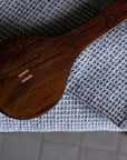 A close-up of a dark brown wooden brush with a small double-stripe logo, resting on a gray waffle-knit blanket.