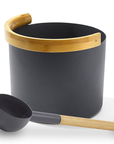 Black aluminum sauna bucket with curved bamboo handle and a matching ladle next to it against a white background