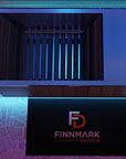 A modern overhead view of a dark wooden slatted cold plunge tub, with blue accent lighting. Below it is a black sign displaying the logo and name 'FINNMARK DESIGNS'.