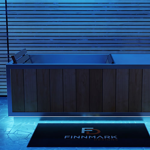 A modern rectangular cold plunge with a dark wood-paneled front and light blue interior, shown in a blue-lit bathroom setting with a black FINMARK DESIGNS floor mat in front.