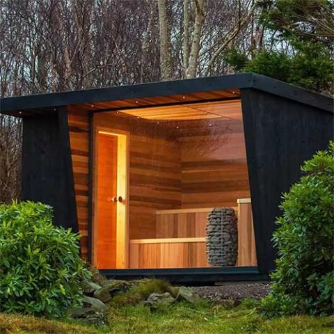 Modern outdoor cabin with wooden interior and black exterior, surrounded by trees and greenery.