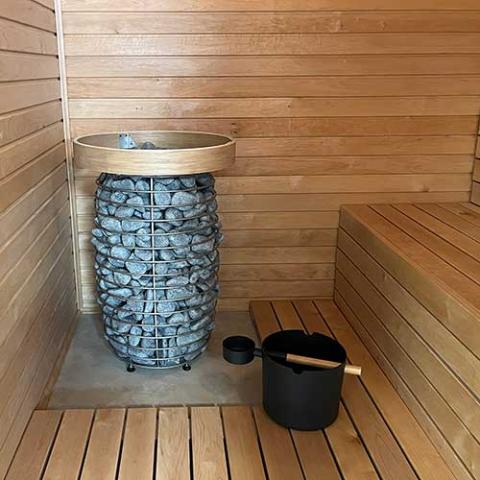 Wooden sauna with a stone-lined water bowl and black pot on a wooden floor.