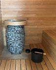 Wooden sauna with a stone-lined water bowl and black pot on a wooden floor.