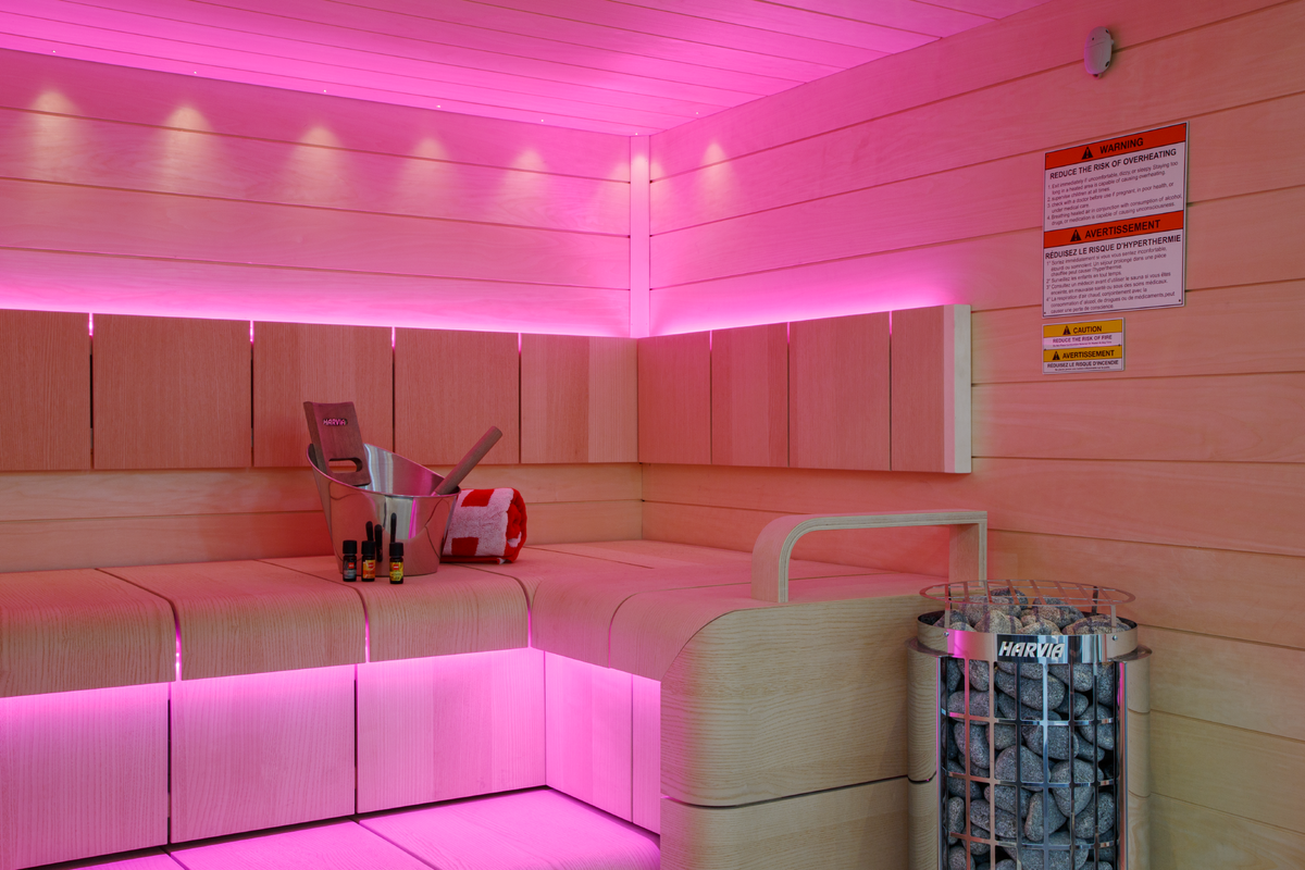 Harvia Cilindro Sauna Heater sauna interior with pink accent lighting with 2 bench levels and bucket with folded towel and oils