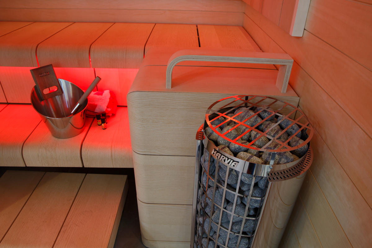 Harvia Cilindro Sauna Heater sauna interior close up heater filled with stones with 2 bench levels and bucket with folded towel