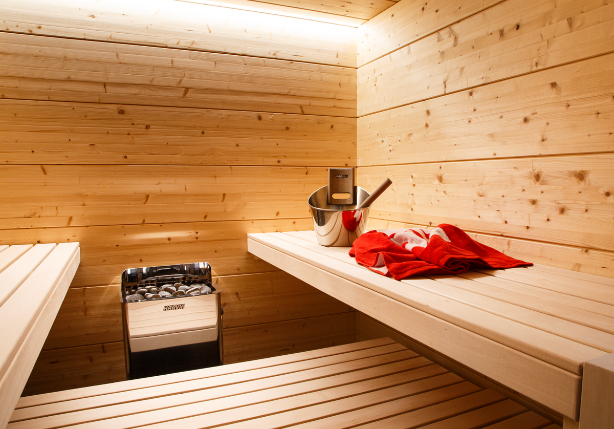 Harvia The Wall Sauna Heater Stainless Steel mounted on sauna wall with bucket and towel on bench