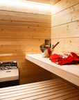 Harvia The Wall Sauna Heater Stainless Steel mounted on sauna wall with bucket and towel on bench