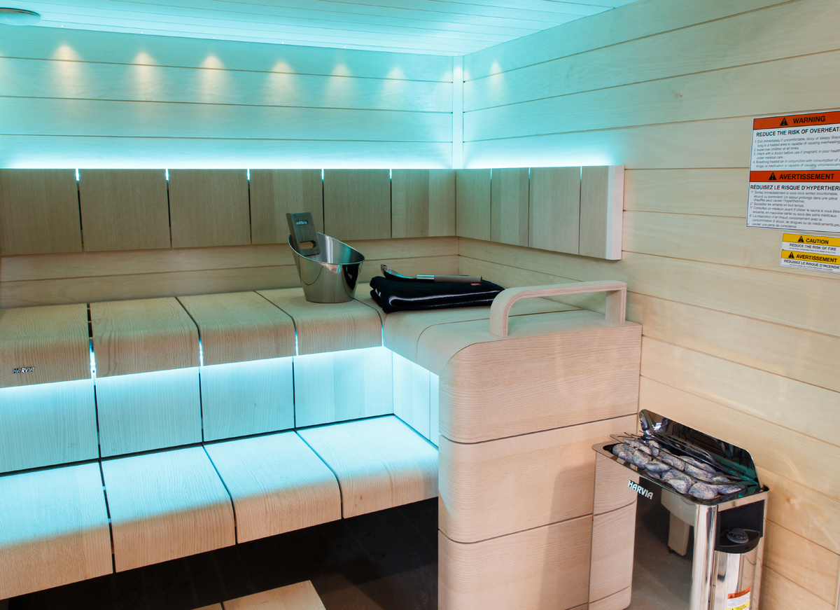 Harvia The Wall Sauna Heater Stainless Steel mounted on sauna wall full view with stones underneath stainless steel grate sauna interior with light blue indirect LED lighting