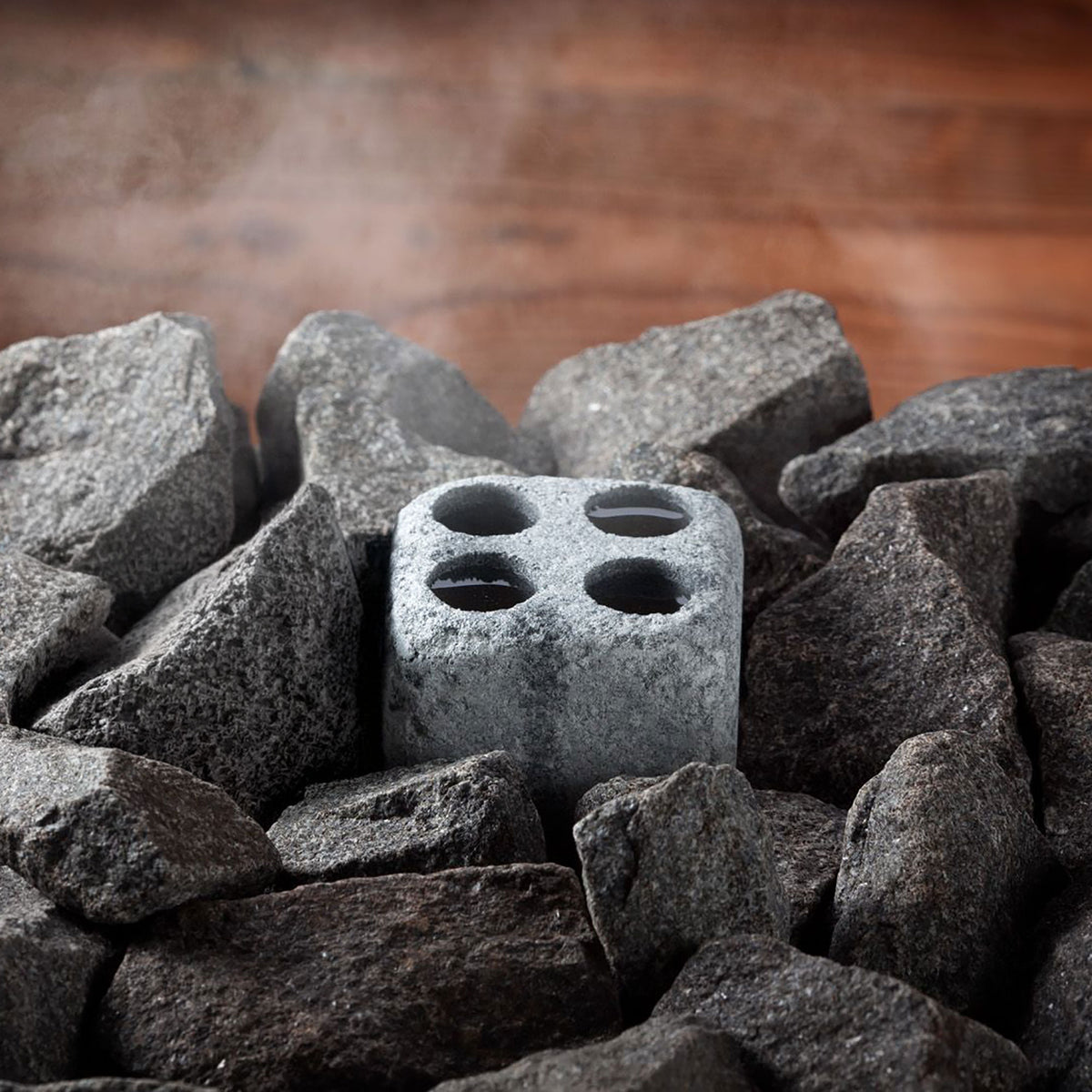 sauna steam stone with four holes surrounded by larger stones on a wooden surface