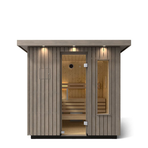 Kohler C2 Sauna Weathered Spruce exterior front view with indirect lighting on the eaves and a clear glass door