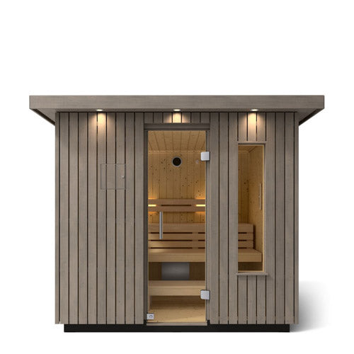 Kohler C2 Sauna Weathered Spruce exterior front view with indirect lighting on the eaves and a clear glass door