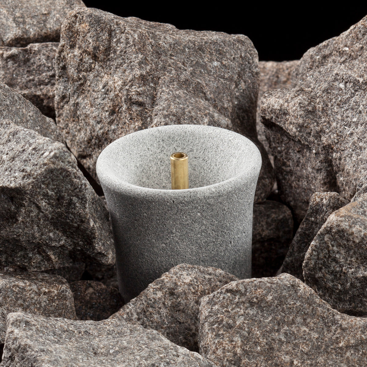 grey sauna stone with a cylindrical hole in a pile of heater stones