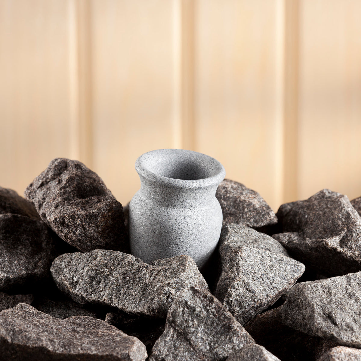 light grey sauna stone sitting amongst dark grey heater stones against a wood background