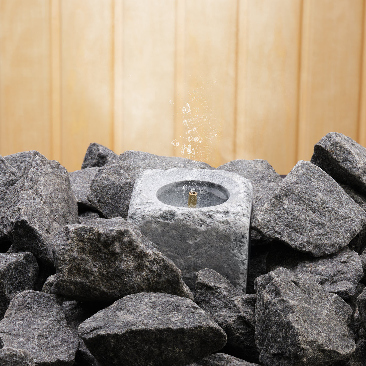 sauna stone fountain with water and steam coming out the top in between dark grey sauna stones on a wooden background