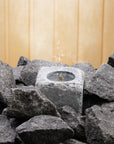 sauna stone fountain with water and steam coming out the top in between dark grey sauna stones on a wooden background