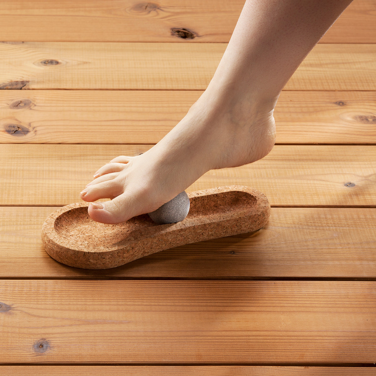 Person stepping onto a cork footrest with a sauna stone on a wooden floor