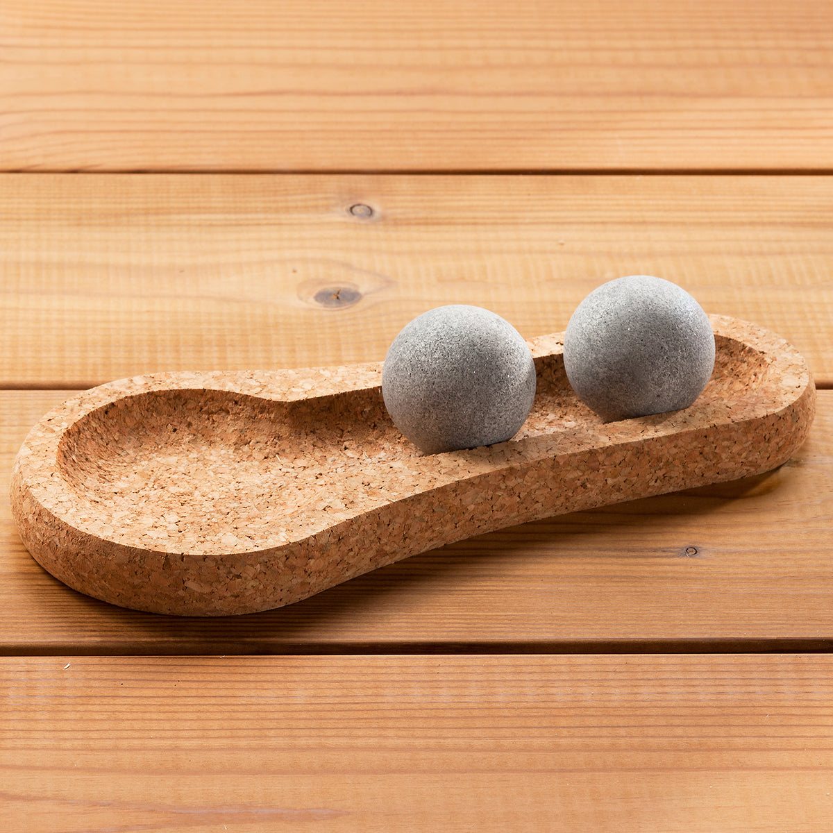 Cork tray with two gray spherical objects on a wooden surface