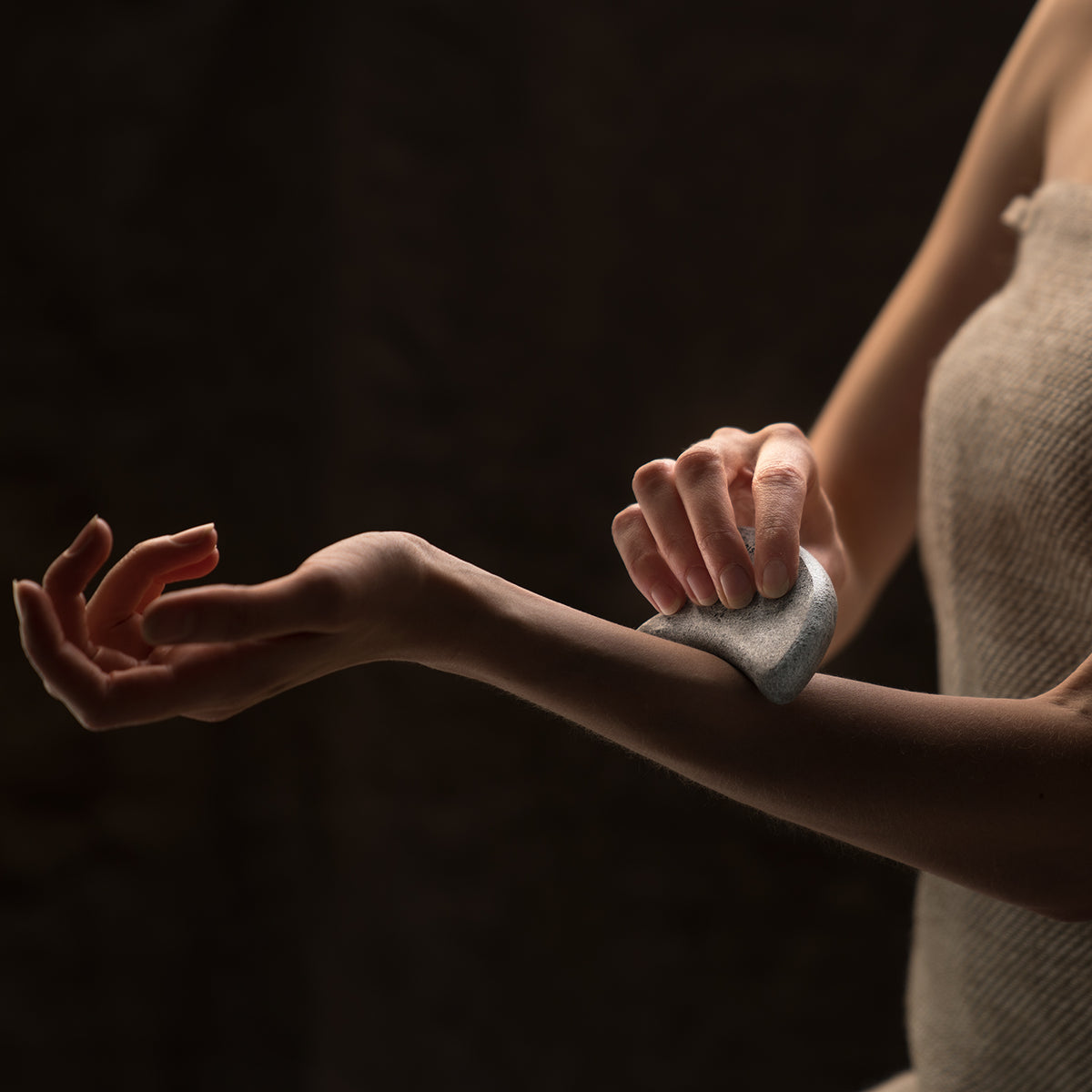 Person rubbing a guasha sauna stone to their arm against a dark background