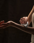 Person rubbing a guasha sauna stone to their arm against a dark background