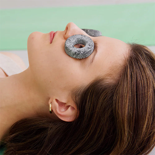 Woman receiving a stone facial treatment with a green background