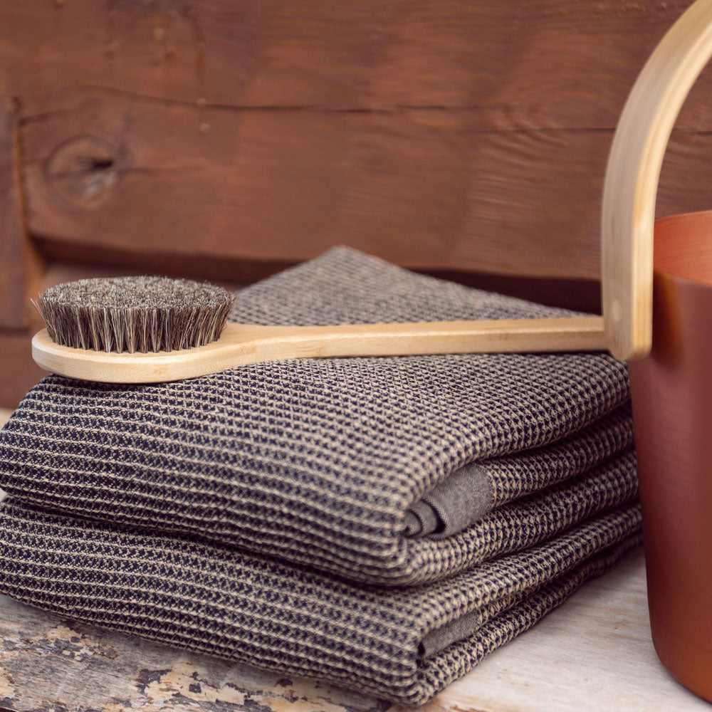 Stack of folded gray towels with a wooden brush on top, against a wooden background.