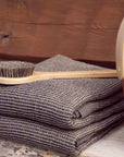 Stack of folded gray towels with a wooden brush on top, against a wooden background.