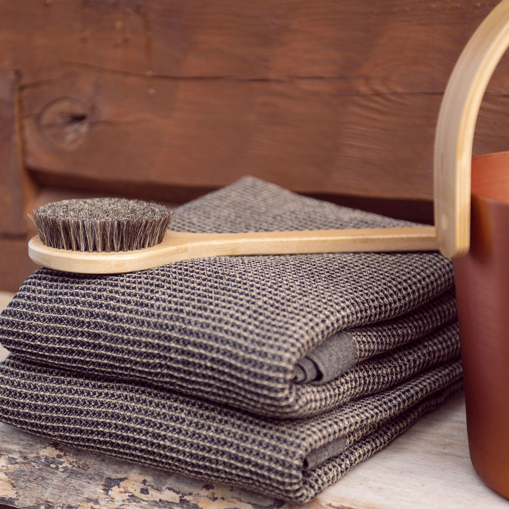 folded brown towel on a wooden bench and a long natural wood brush on top. terracotta bucket and natural wood handle sit next to the towel
