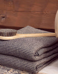 folded brown towel on a wooden bench and a long natural wood brush on top. terracotta bucket and natural wood handle sit next to the towel