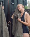 Woman drying off with a towel outdoors next to stacked wood