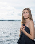 women standing with dark grey textured towel wrapped around her with a lake behind her and trees in the distance