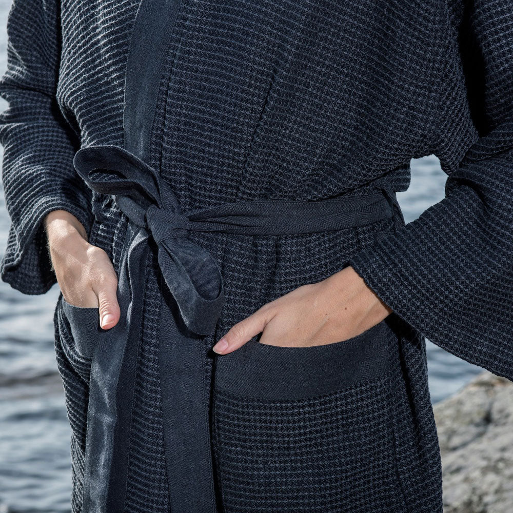 Person wearing a dark textured sauna robe by a body of water