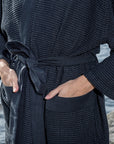 Person wearing a dark textured sauna robe by a body of water