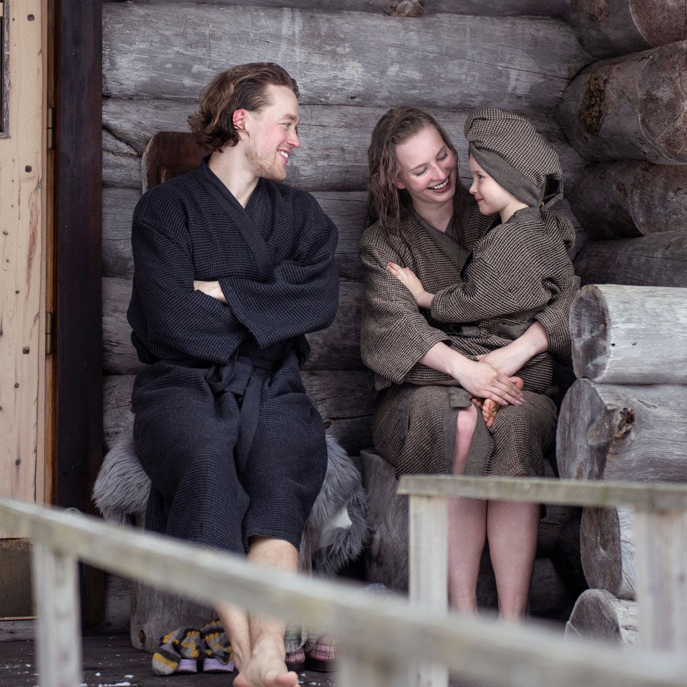 Three people in sauna robes sitting together in a wooden sauna.
