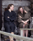 Three people in sauna robes sitting together in a wooden sauna.